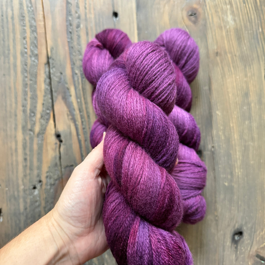 A skein of tonal purple yarn held by a light-skinned hand.