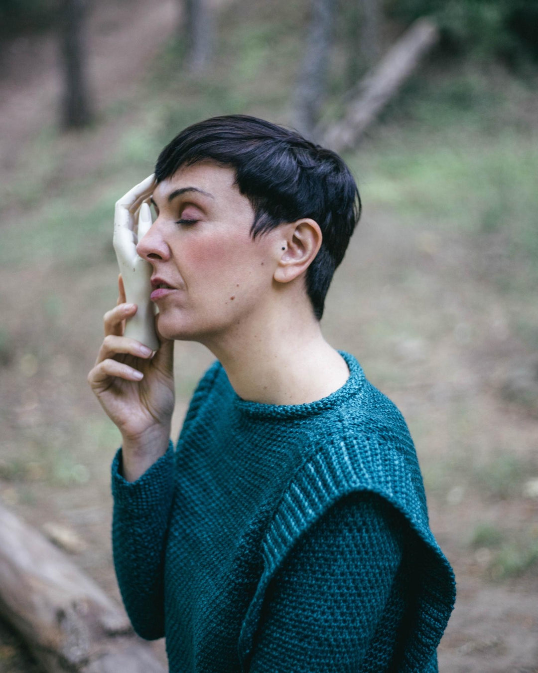 A model wearing a teal textured sweater with a large ruffle at the shoulders.