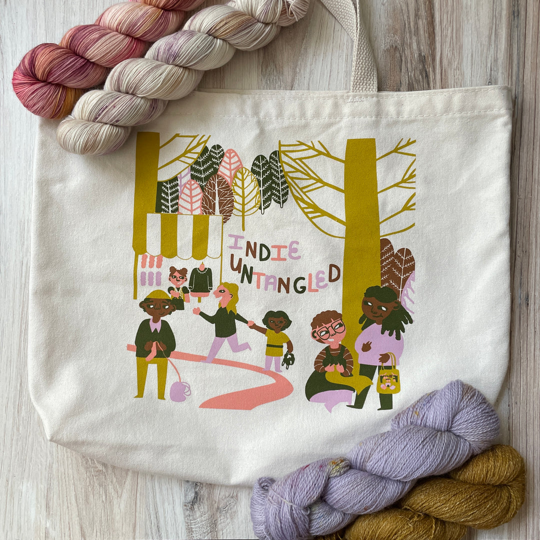 A cream tote bag with a gold, brown, pink, purple and gray illustration.