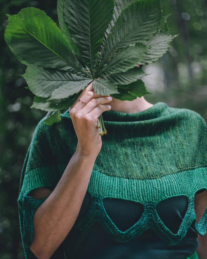 A model wearing a green knit shawl with large diamonds cut out.