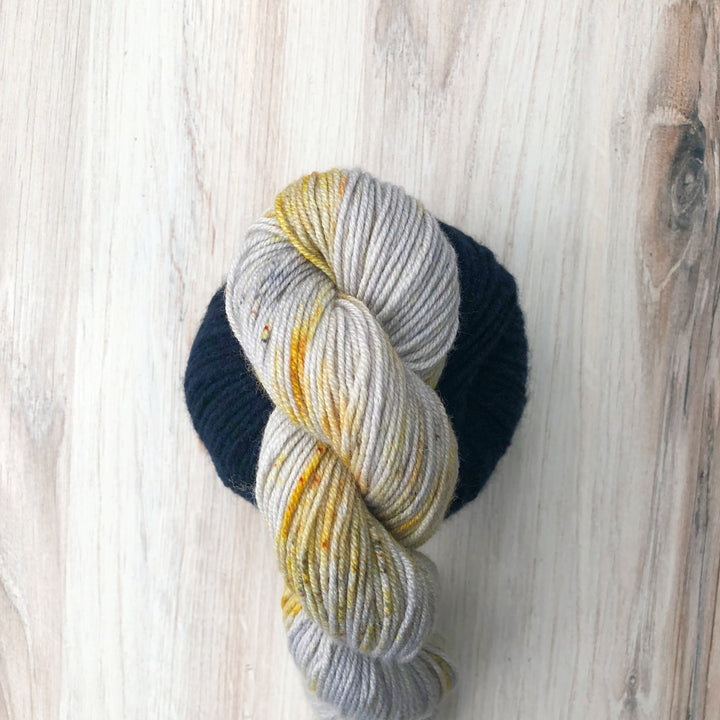 A twisted skein of silver yarn with gold speckles above a ball of navy yarn.
