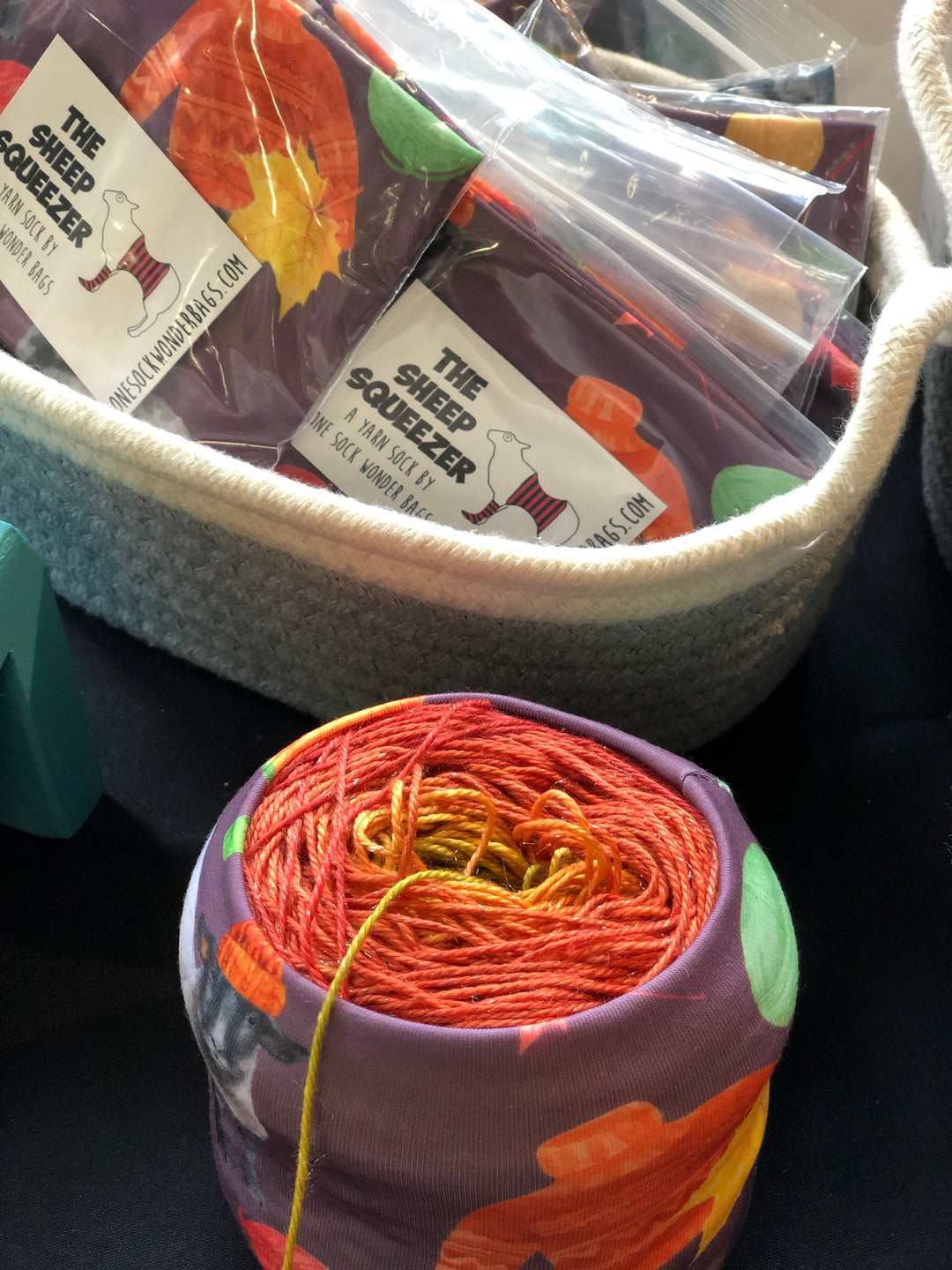 A purple, orange and green sleeve holding a cake of red to green ombre yarn.