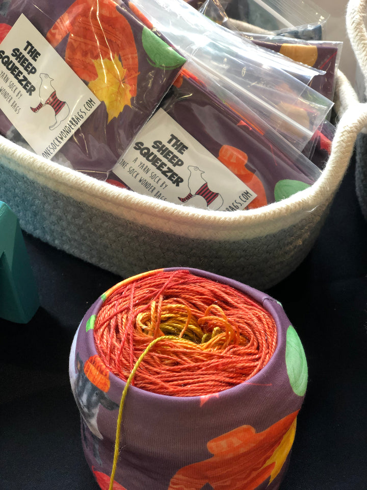 A purple, orange and green sleeve holding a cake of red to green ombre yarn.