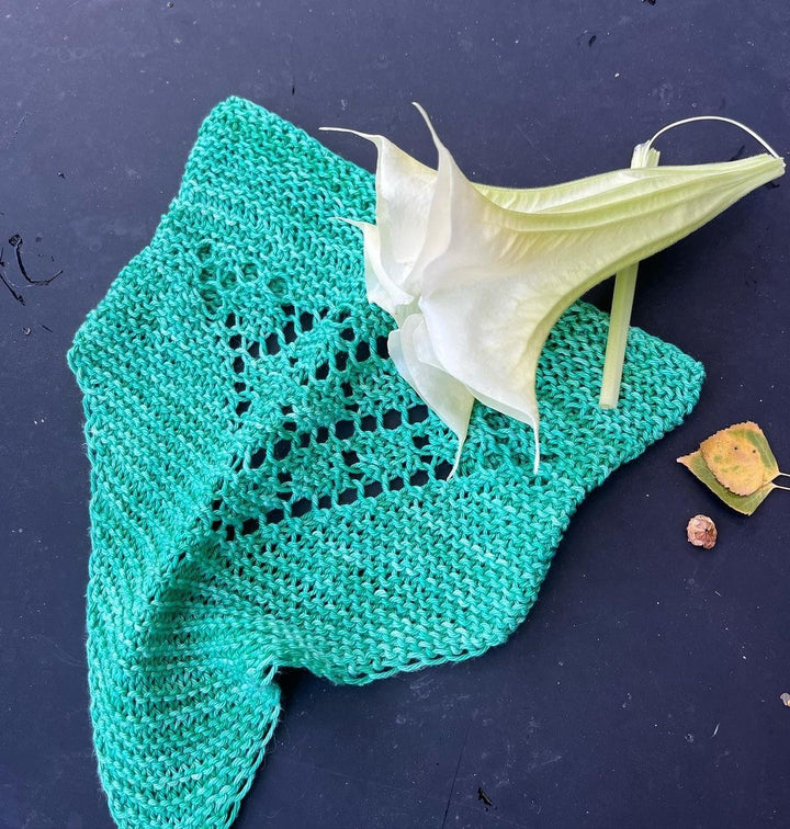 A green knit kerchief with a lace panel and white flower.