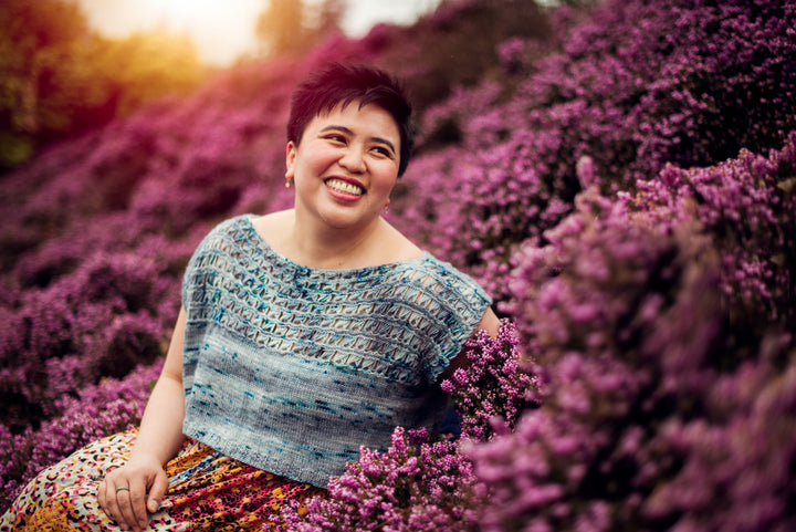 An olive skinned woman wears a blue speckled short sleeved top with lace.