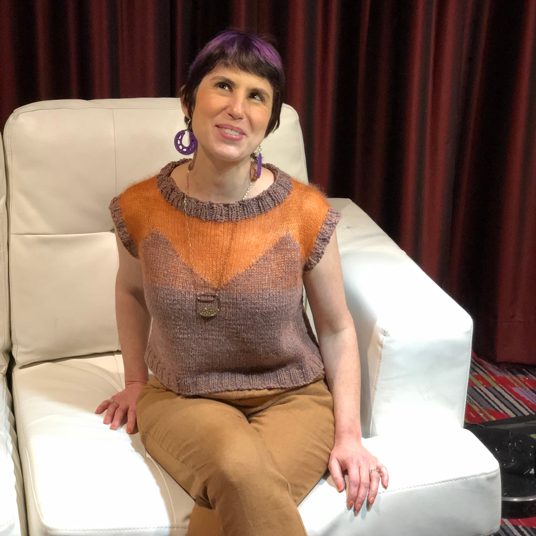 A white woman wears a dusty pink and orange short sleeved sweater.