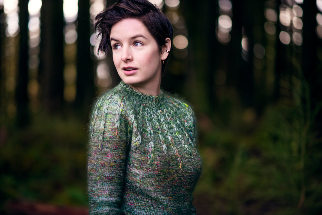 A white woman wears a green speckled ombre sweater.