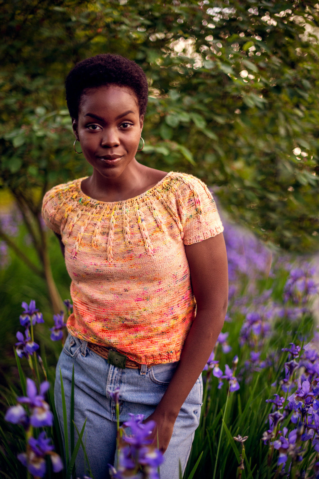 A Black woman wears a bright orange short sleeved sweater.