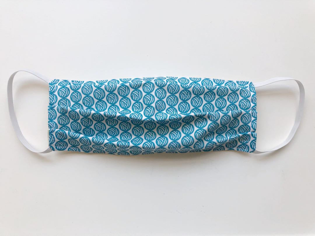A face mask with teal yarn balls.