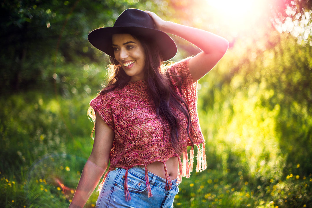 A tan woman wears a lacy pink cropped top with fringe.