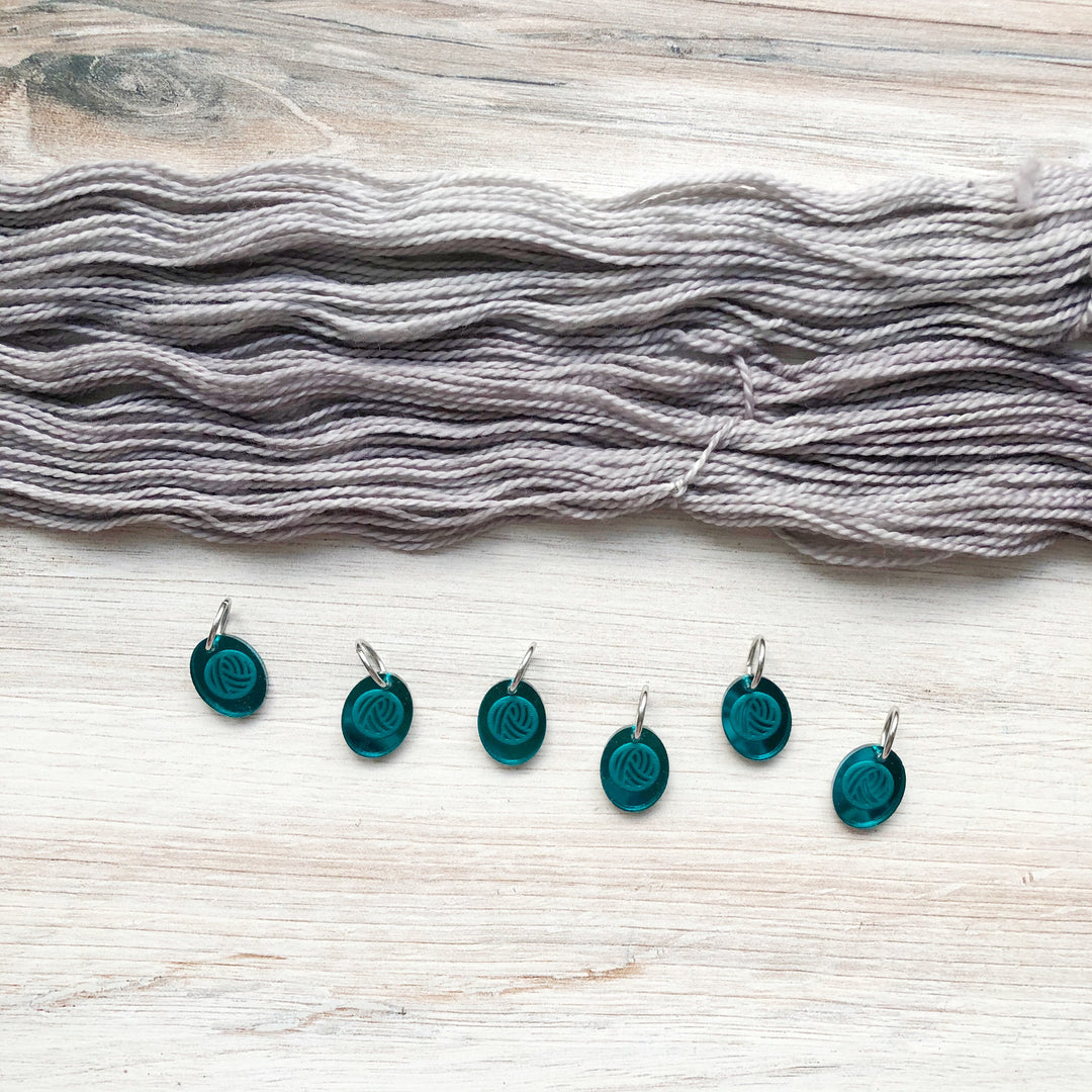 Gray yarn and teal mirrored stitch markers. 