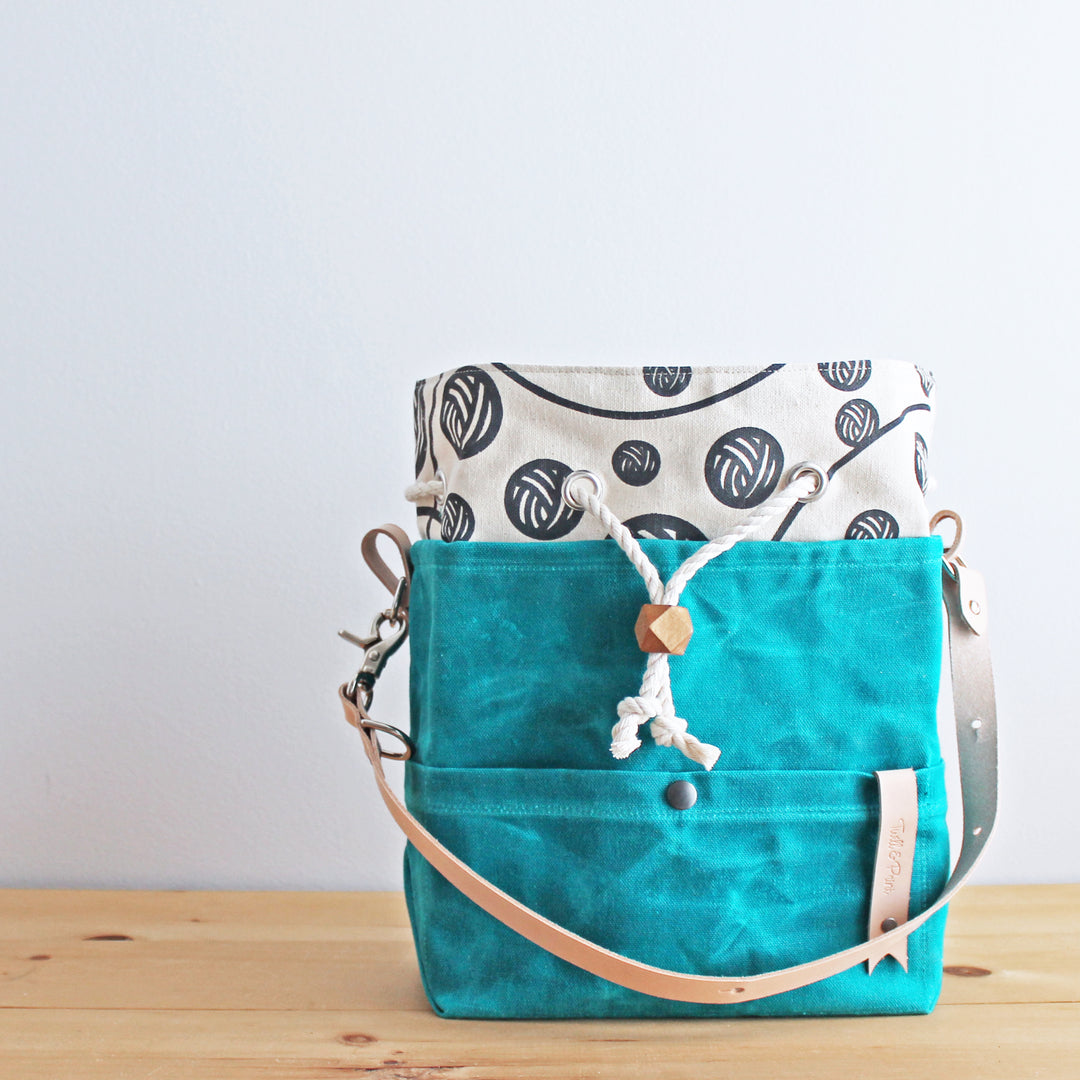 A turquoise bag with a yarn ball print in gray.