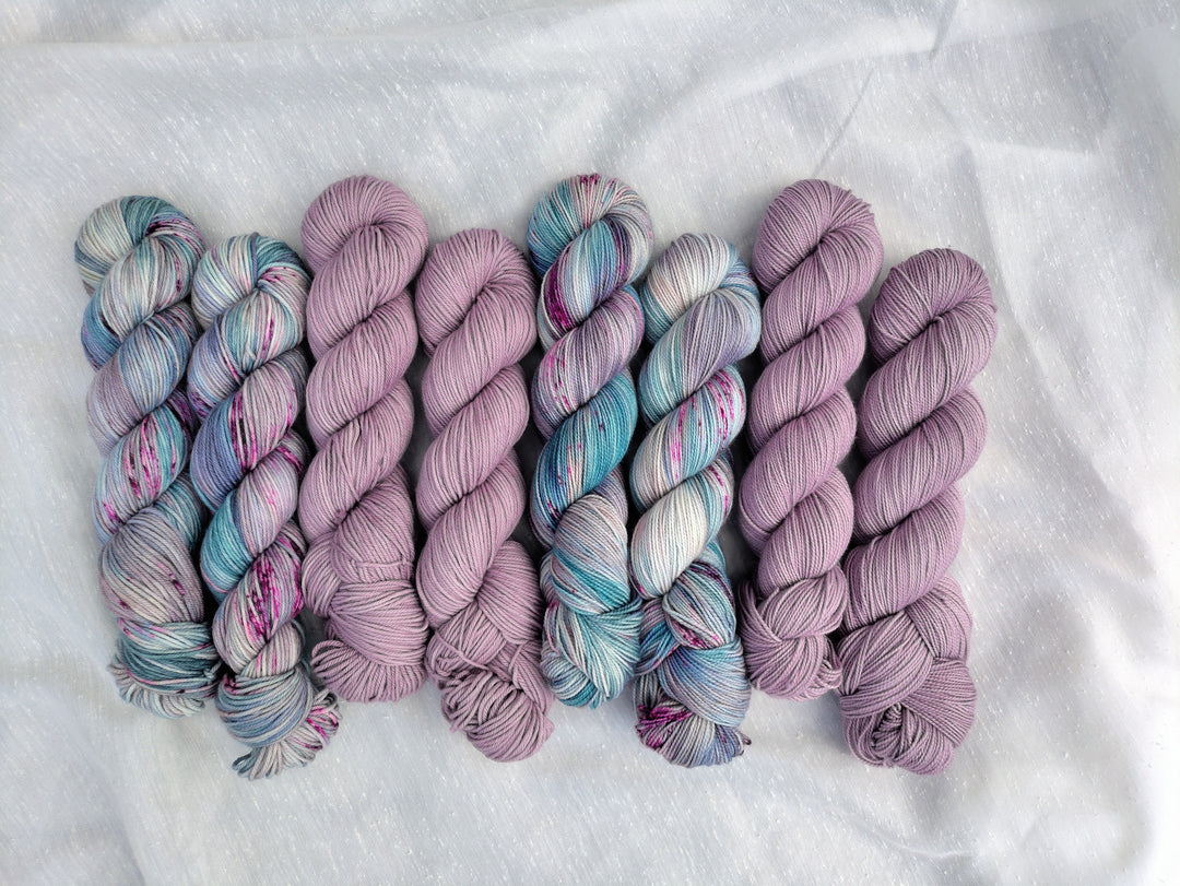 Blue, purple and green speckled yarn and pale purple semisolid yarn.