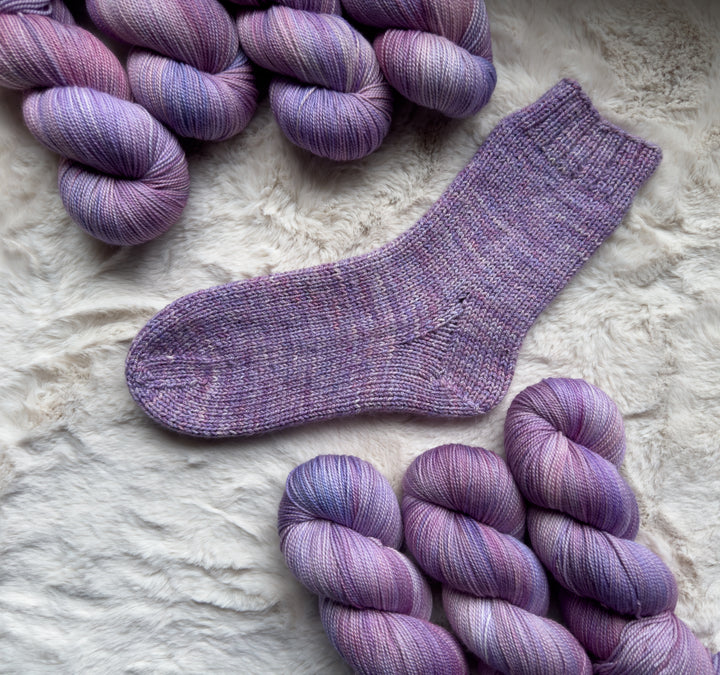 Purple and pink hand-dyed yarn and a knit sock in the same colors.