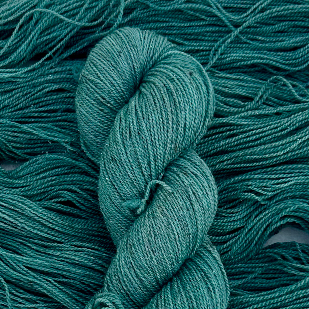 A twisted skein over a loose skein of blue/green yarn.