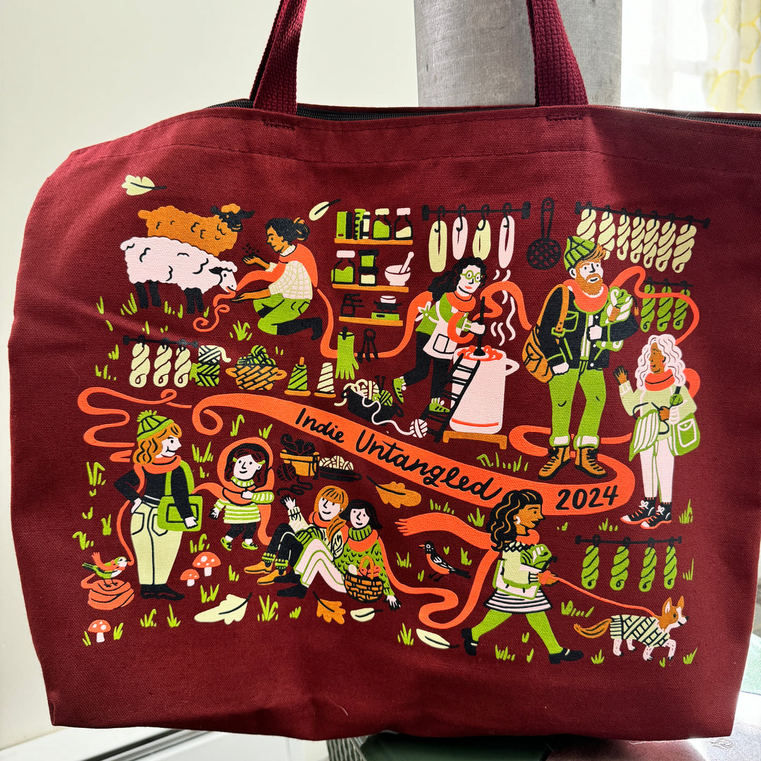 A tote bag with a green, orange and pink illustration for Indie Untangled 2024.