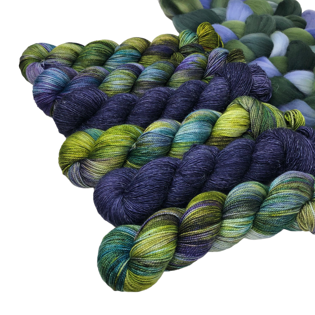 Skeins of hand-dyed yarn in various shades of green, blue, and purple and a close-up of braided fiber in similar colors.