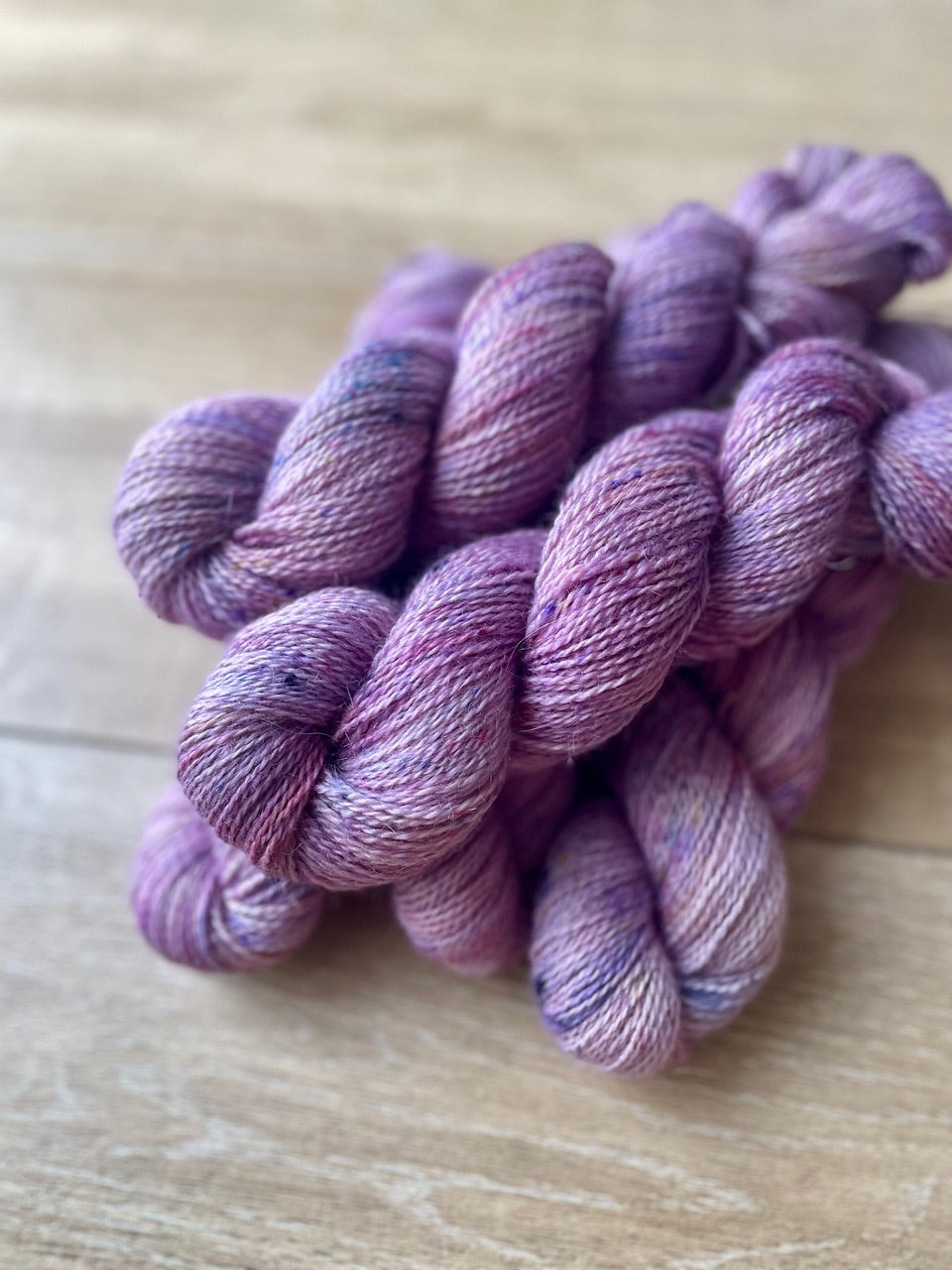 Skeins of hand-dyed yarn in a soft lavender color with speckles of pink and purple throughout.