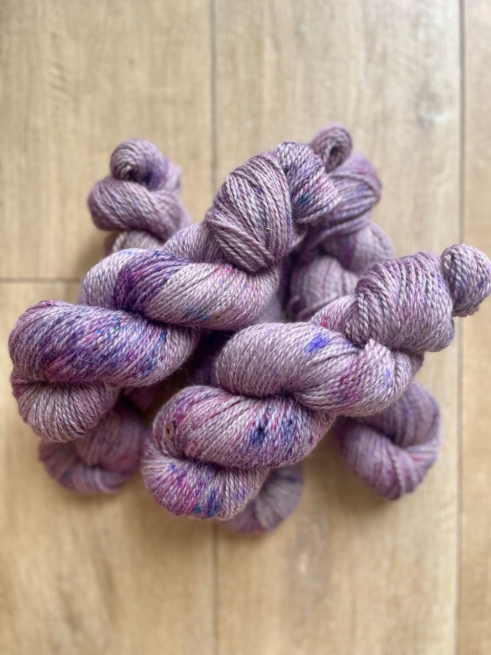 Skeins of hand-dyed yarn in a soft lavender color with speckles of pink and purple throughout.