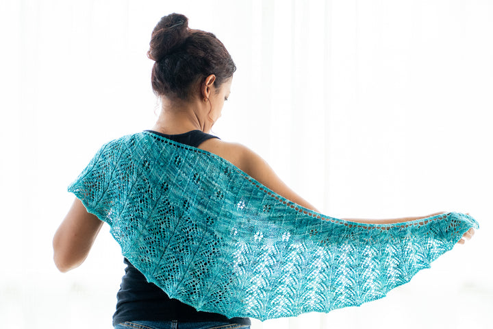 A brown-skinned woman holding up a blue-green lace shawl.