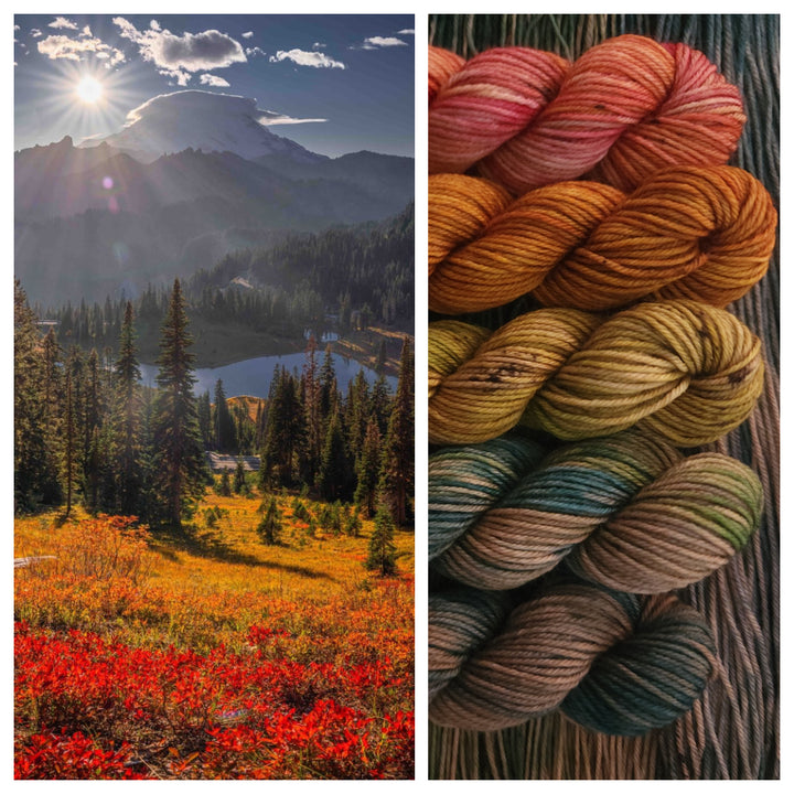 A scenic landscape with a sunlit mountain, a forest, a lake and vibrant autumn foliage in shades of red and orange. Five mini skeins of hand-dyed yarn, echoing the autumn colors of the landscape.