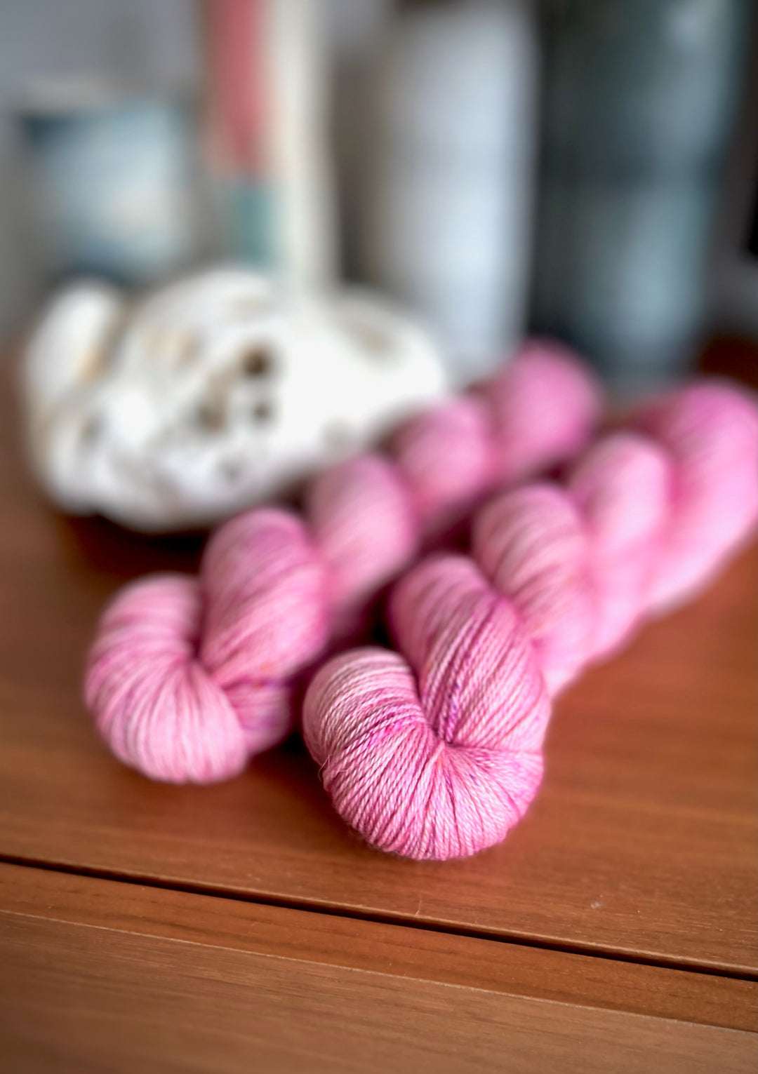 Skeins of pink lightly speckled yarn with a blurred background.