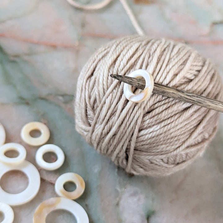 A closeup of a seashell stitch marker on a wooden needle. 