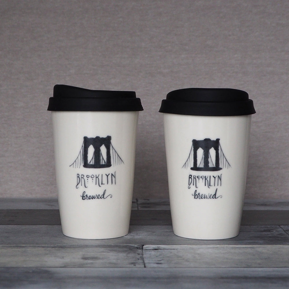 Two cream cups with black covers and an illustration of the Brooklyn Bridge and the words Brooklyn Brewed.