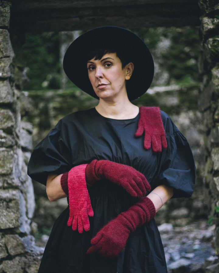 A model in a black dress wearing and draped with red knit gloves.