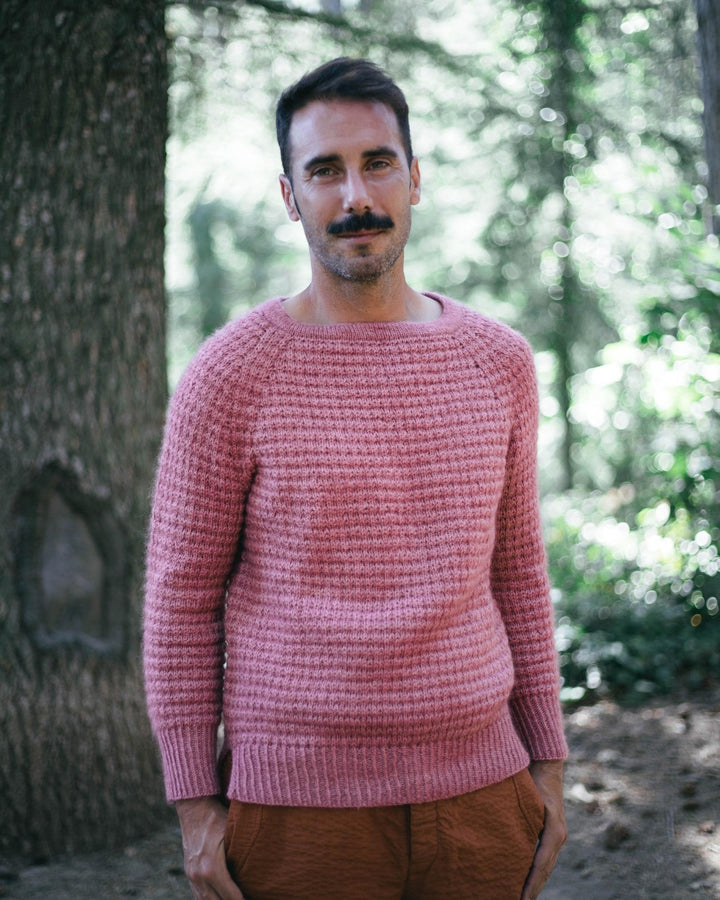 A man with a mustache wears a pink textured sweater.