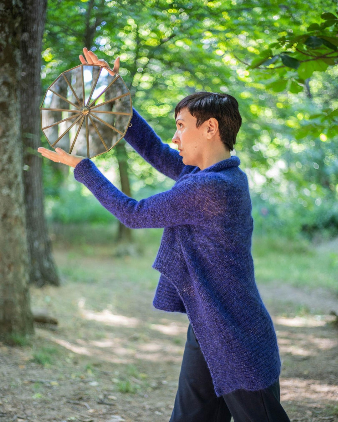 A model holding a prism disc wearing a draped blue cardigan. 