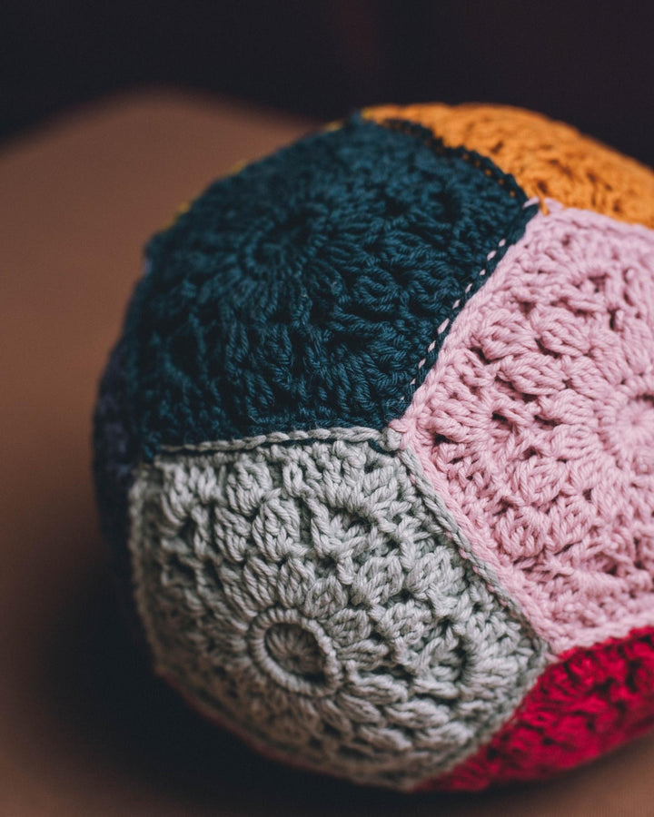 A crocheted ball in teal, gray, pink, yellow and red trapezoids. 