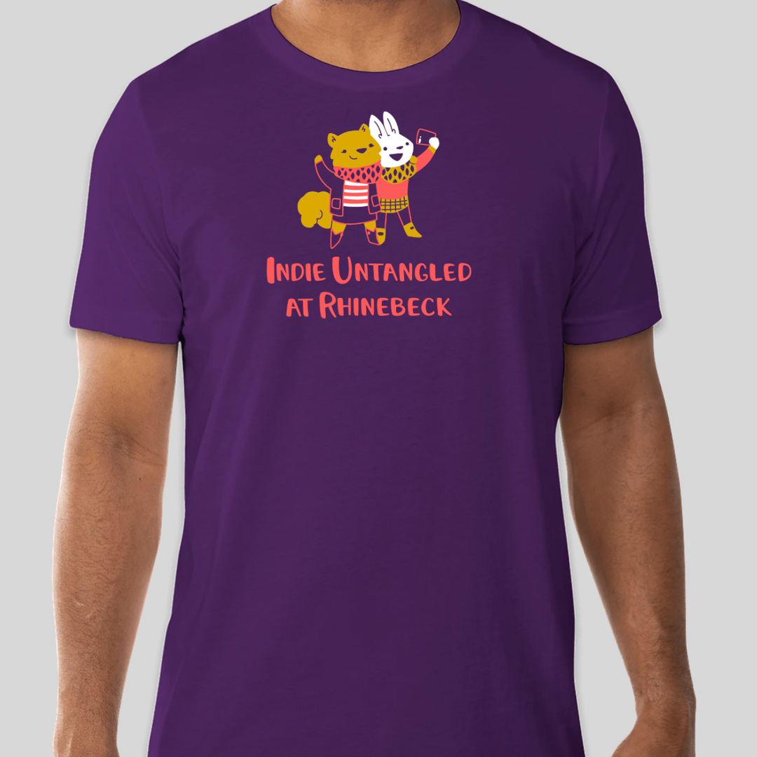 A purple T-shirt with an illustration of a yellow squirrel and white bunny taking a selfie above the words Indie Untangled At Rhinebeck in coral.