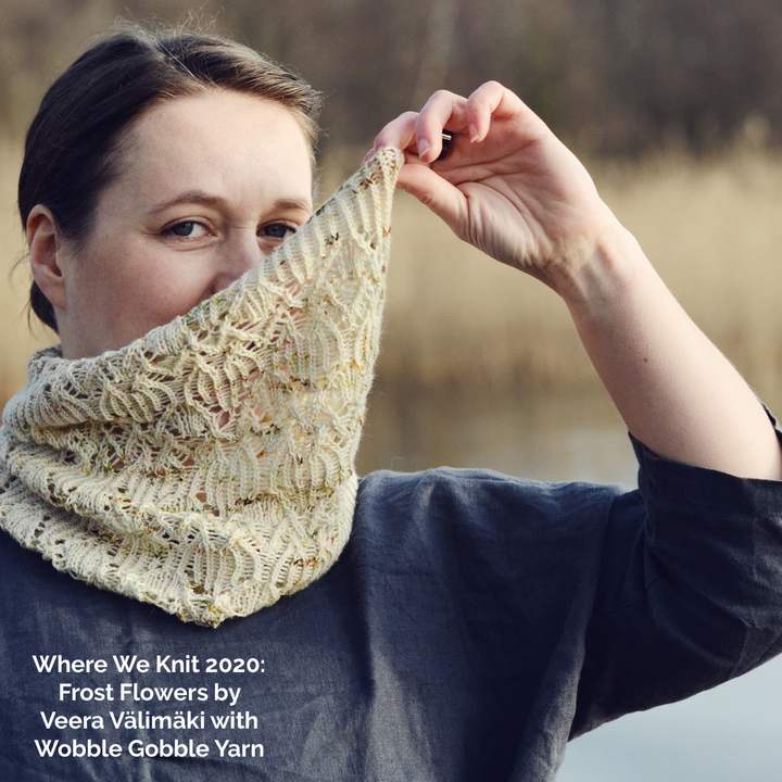 A woman holds up a cream colored speckled cowl and the words Where We Knit 2020 Frost Flowers by Veera Valimaki with Wobble Gobble Yarn.