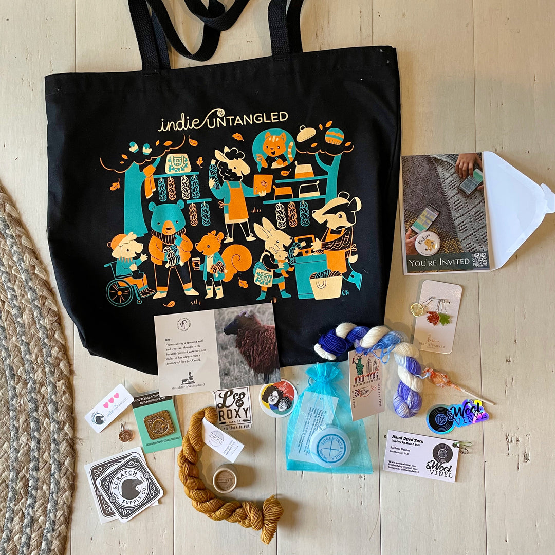 A black tote bag with a teal, orange and cream illustration of human-like animals surrounded by various swag.