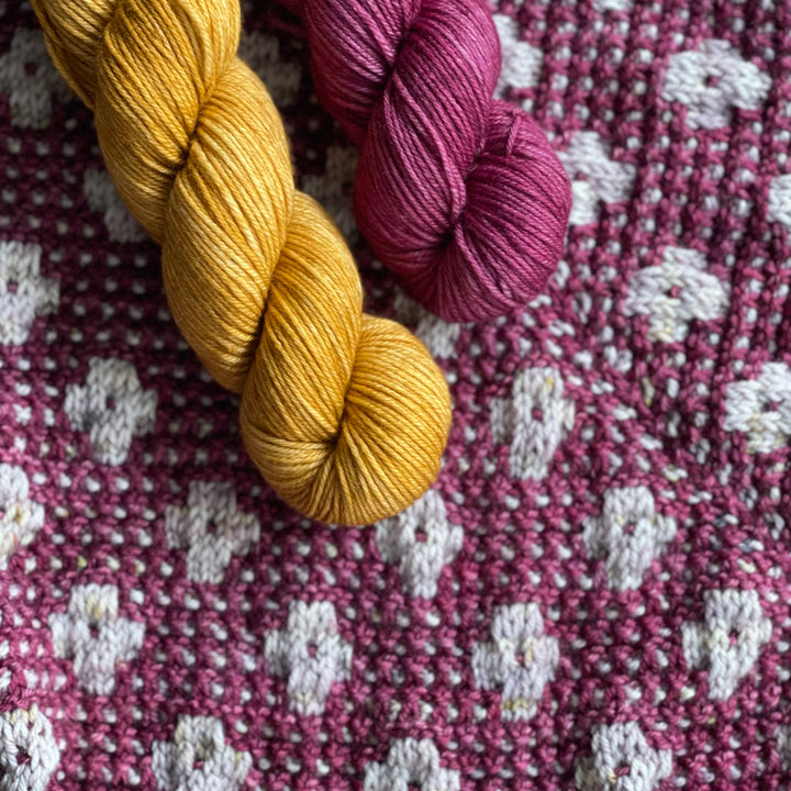 Orange and purple yarn above a gray and purple floral knit pattern.