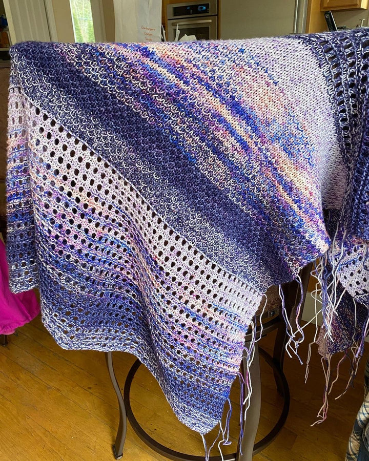 A purple, blue, pink and white shawl with eyelets and textured stitches.