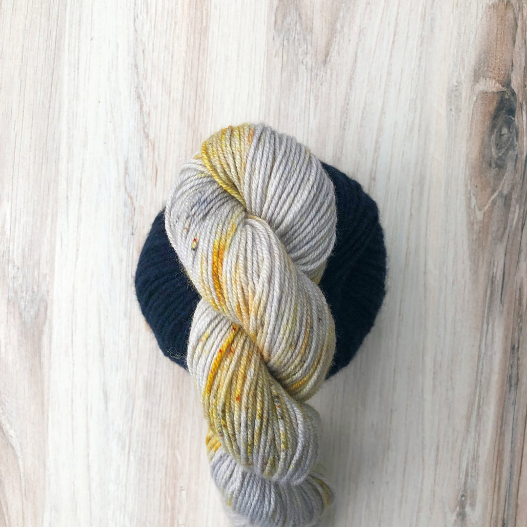 A twisted skein of gray yarn with gold speckles above a ball of navy yarn.