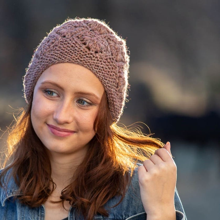 A pale pink knit hat with floral stitches on a white woman with red hair.
