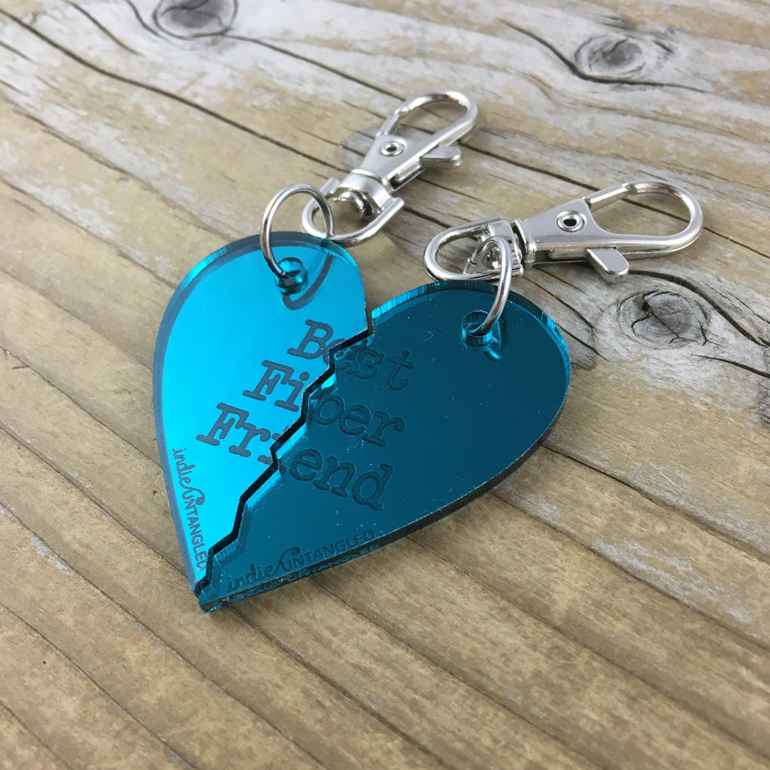 A teal mirrored acrylic heart engraved with the words Best Fiber Friend and the Indie Untangled logo, with silver metal fobs.