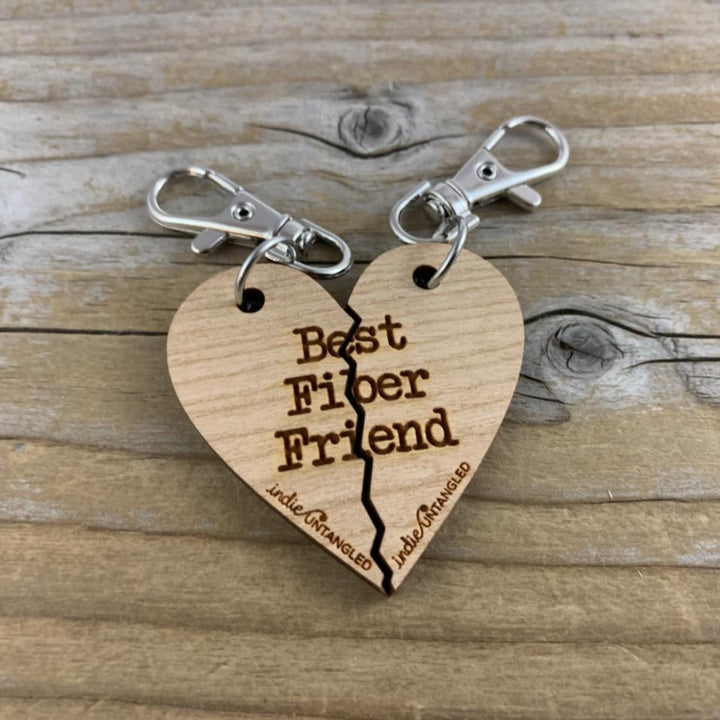A wooden heart engraved with the words Best Fiber Friend and the Indie Untangled logo, with silver metal fobs.
