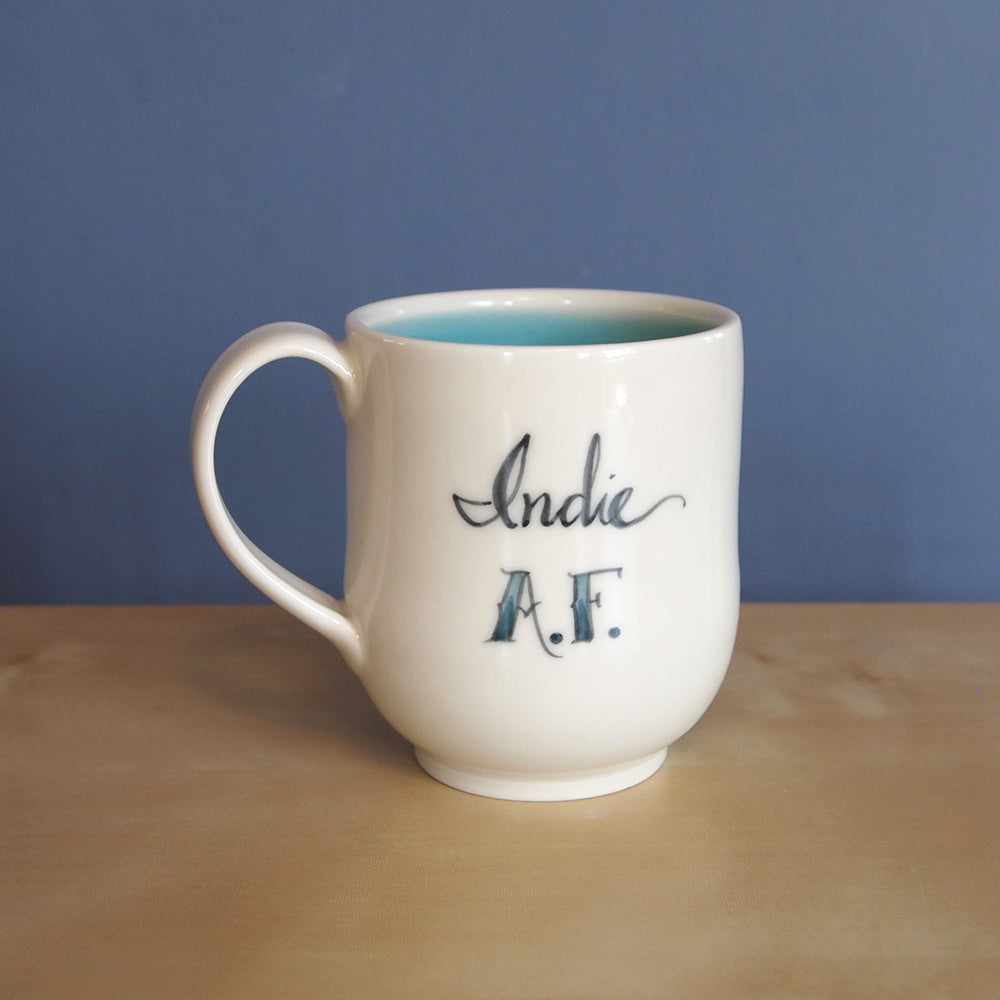 A curved cream mug with the words Indie AF.