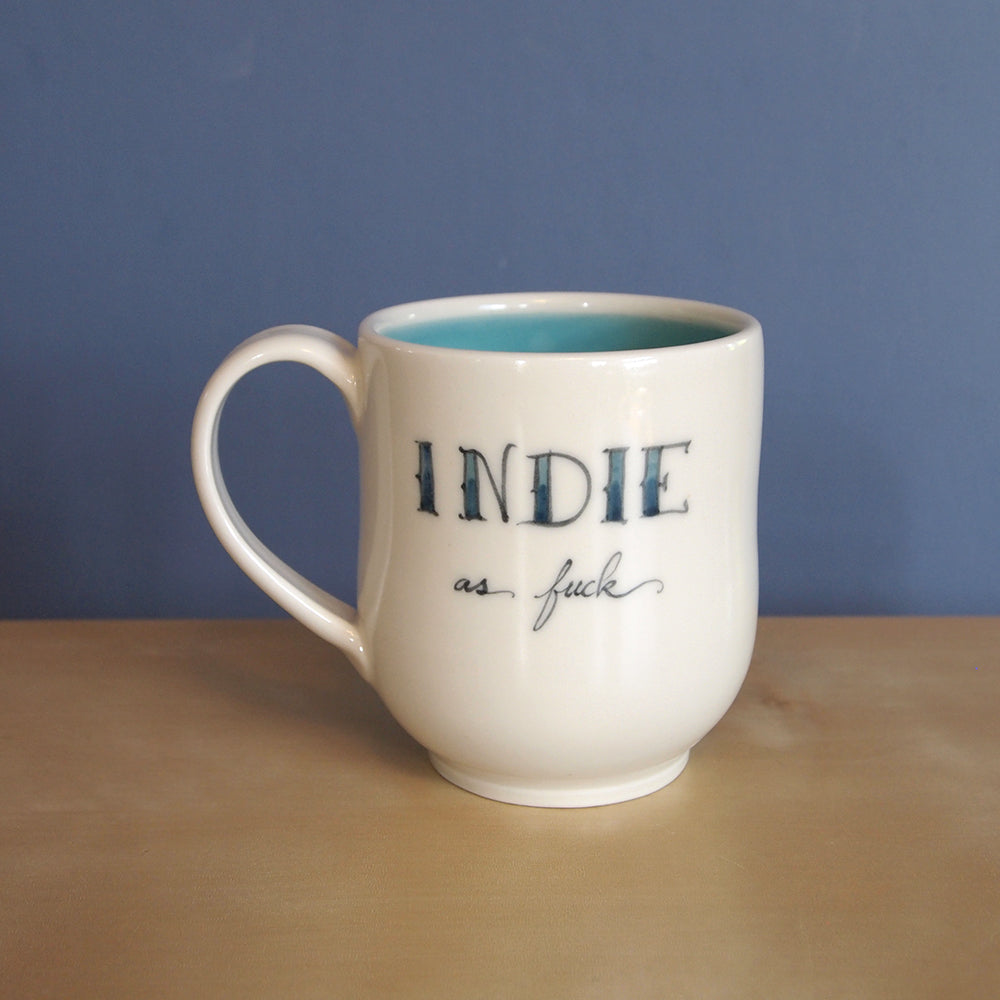 A cream curved mug that reads INDIE as fuck.