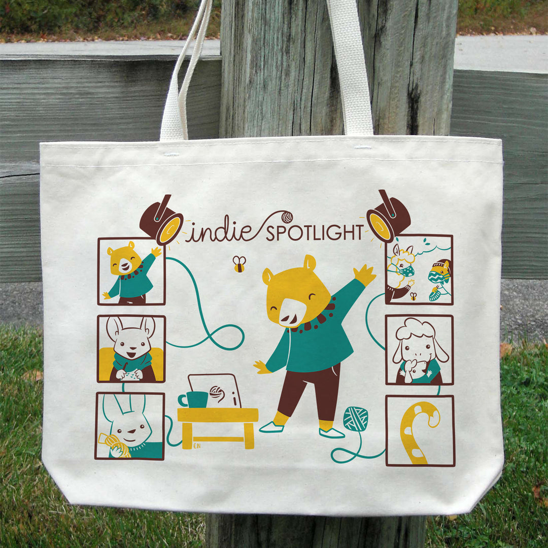 A white tote with an illustration of a yellow bear wearing a teal sweater, surrounded by other animals in squares.