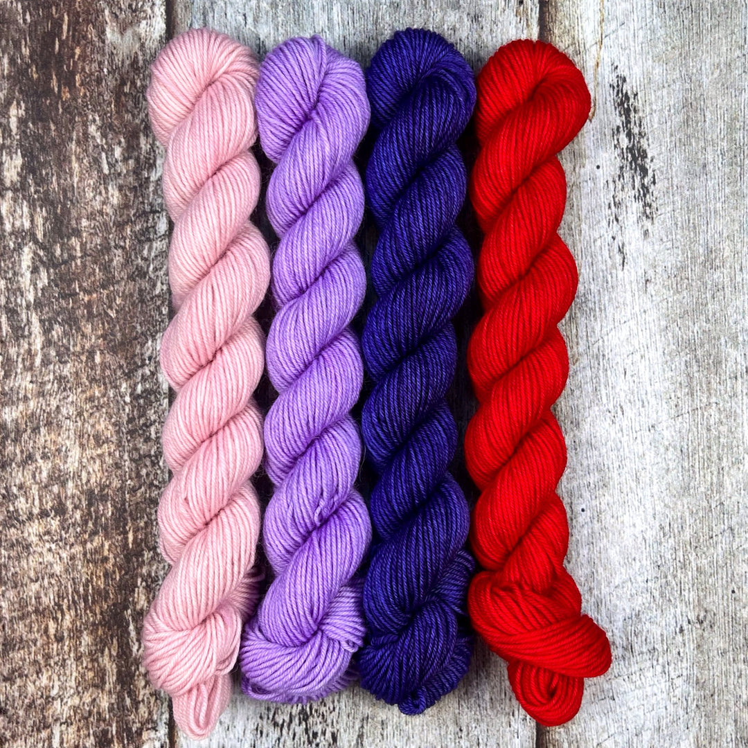 Mini skeins of pale pink, lilac, deep blue and red yarn.
