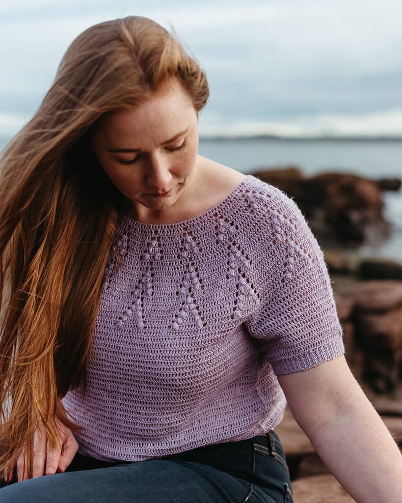 A light-skinned woman wearing a lilac crocheted top.
