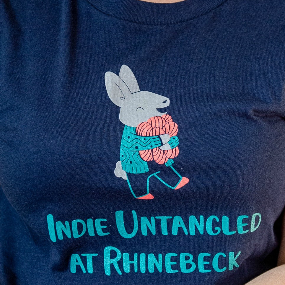 A navy t-shirt with an illustration of a bunny clutching coral yarn and the words Indie Untangled At Rhinebeck.