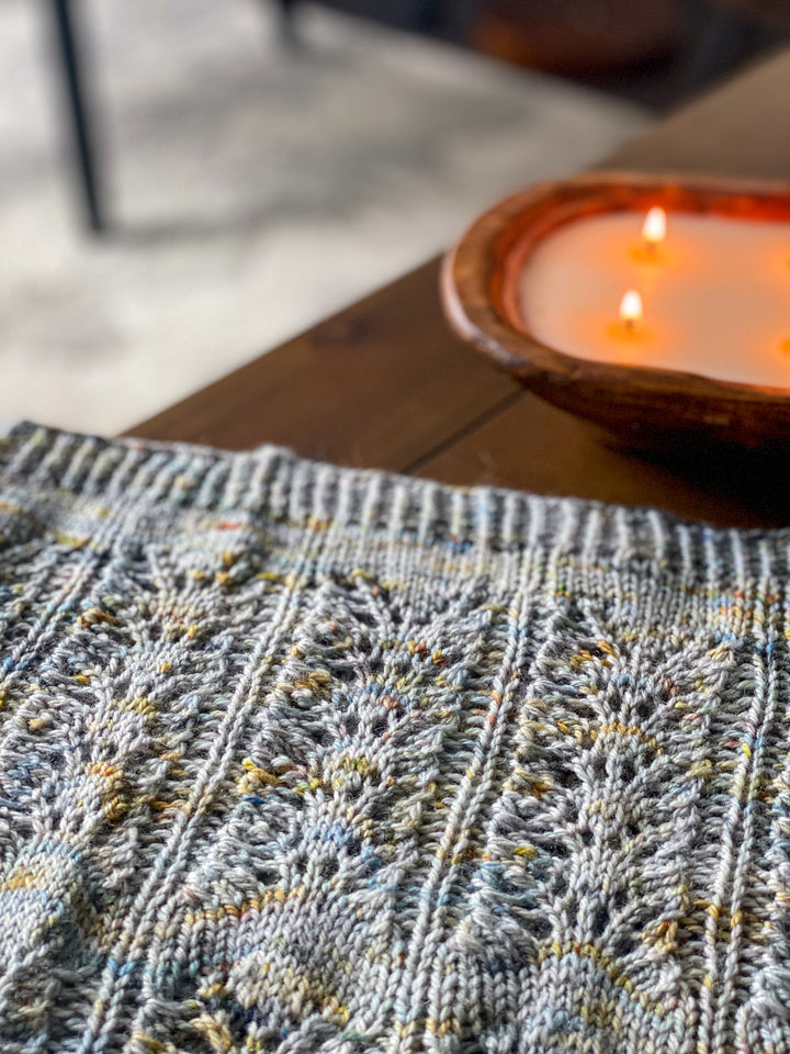 A blue and gold speckled cowl next to a lit candle.