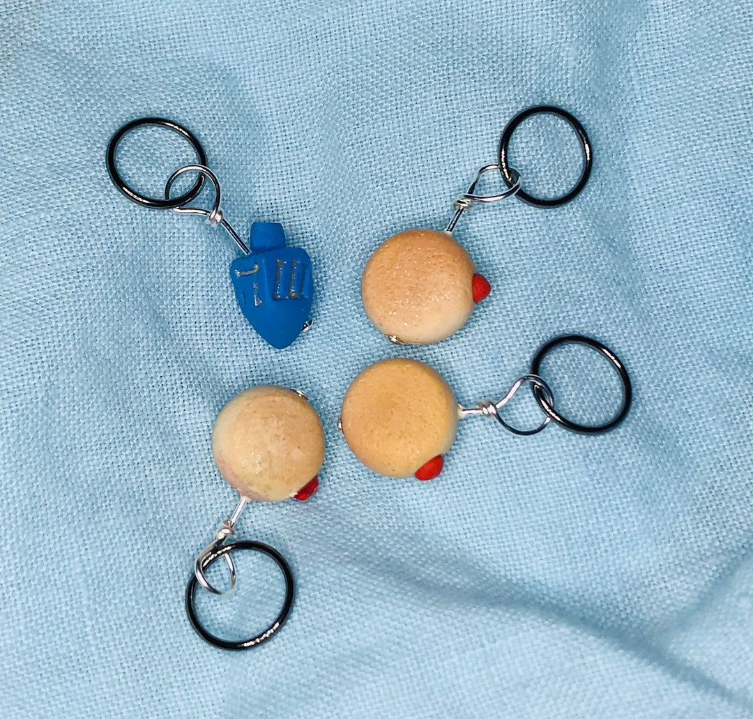 Stitch markers of a blue dreidel and three jelly donuts.