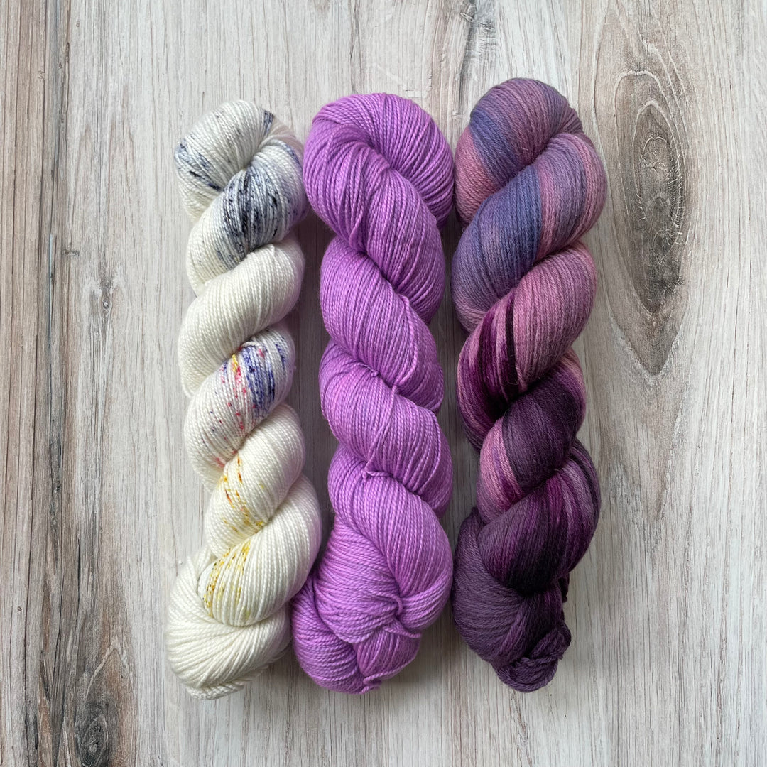 Three skeins of yarn in pink, blue and gold speckle, solid purple and variegated purple. 